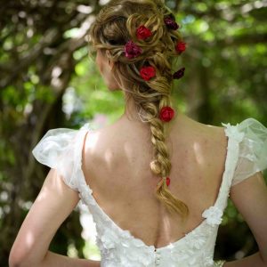 Loose braid adorned with red roses and greenery against a leafy backdrop