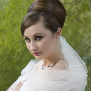 Woman with sophisticated updo hairstyle featuring sleek, voluminous bouffant. Wearing bridal attire, veil and subtle makeup for elegant look