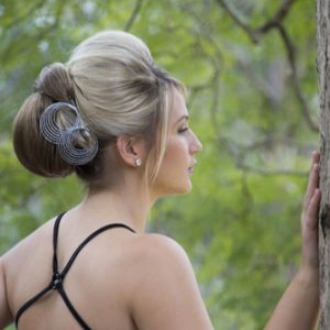 Woman with elegant updo featuring large bun and decorative hair accessory, standing outside near tree in profile view