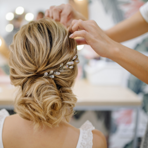 Hairstylist's hands placing elegant gemstone hairpins into elaborate updo on woman with highlighted curly hair for special occasion