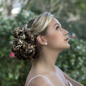 Woman with elegant updo hairstyle of curls and twists, set against blurred natural background